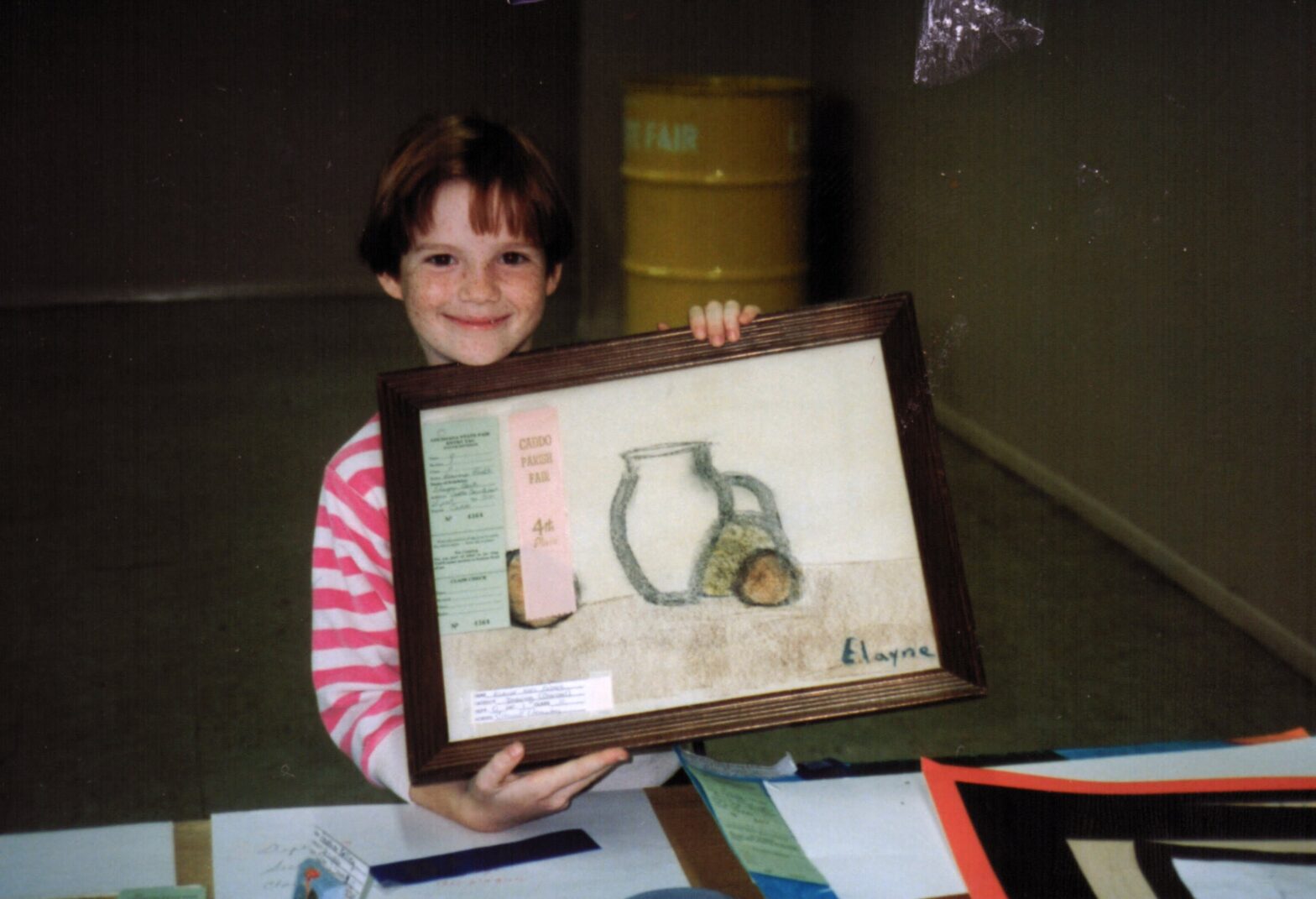 Elayne as a child holding a charcoal sketch of a pitcher and some fruit